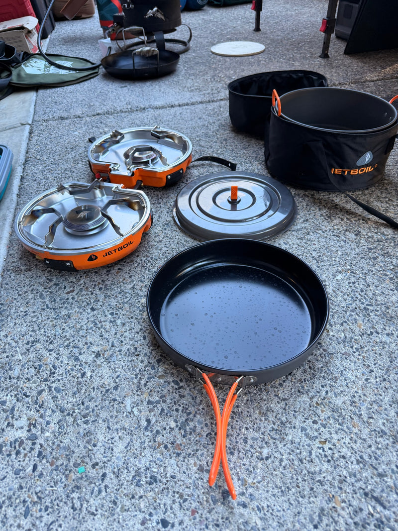 RV rental ready: Jetboil stoves, pan, and camp cookware laid out on concrete, prepared for outdoor cooking. — photo 9