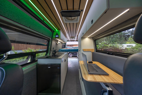 Explore this modern RV rental interior: sleek kitchen, cozy bed, and a laptop-ready workspace, all lit by ambient LEDs.