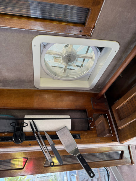 RV rental interior: ceiling vent fan, wooden storage shelf with paper towels & cooking utensils.