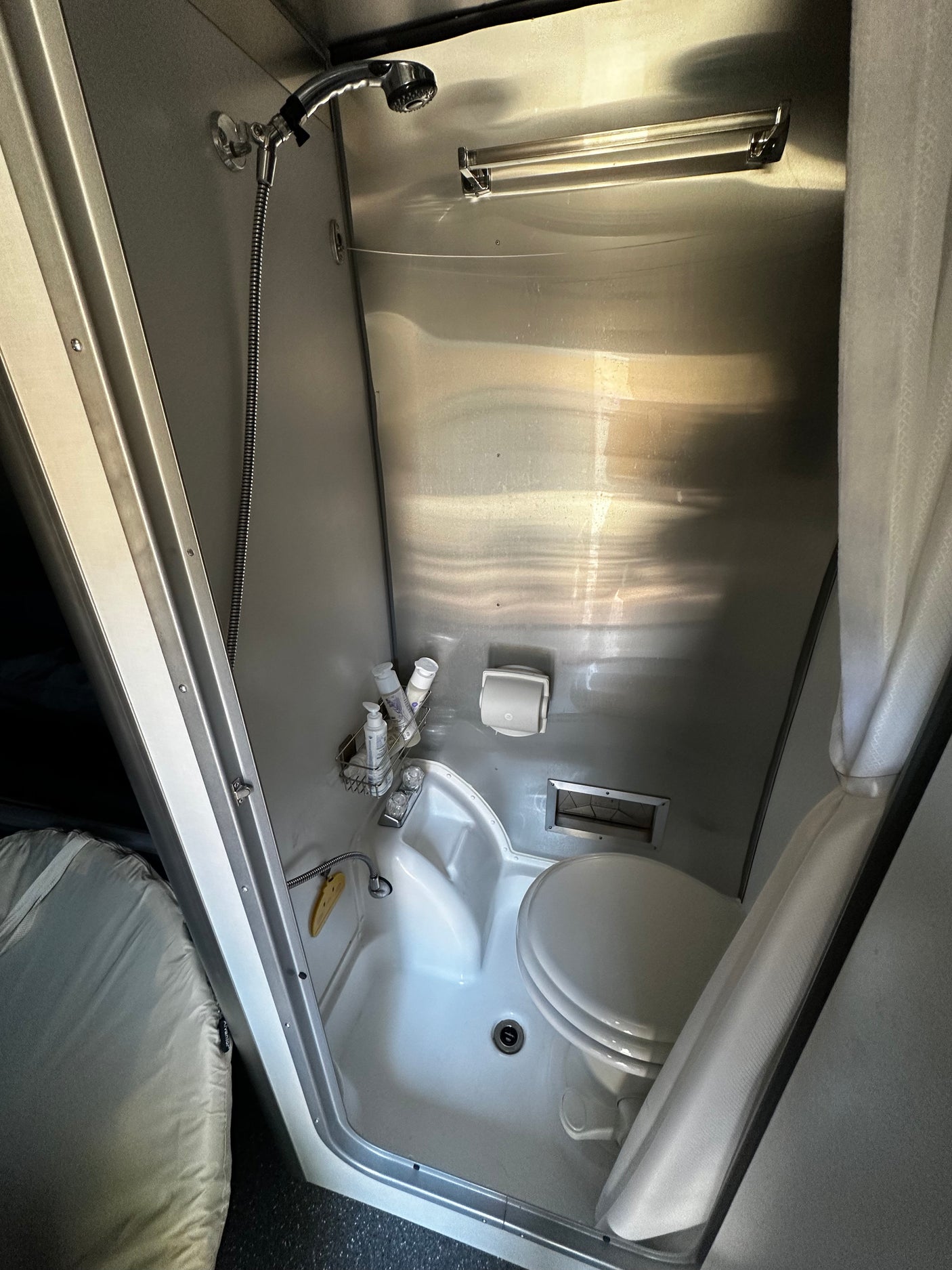 This RV rental's compact wet bath features a shiny metallic interior with a shower, toilet, and sink, optimized for small spaces.