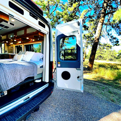 Experience comfort & nature with this rv rental. Inside, a cozy bed and full camper van setup, parked among tall trees.