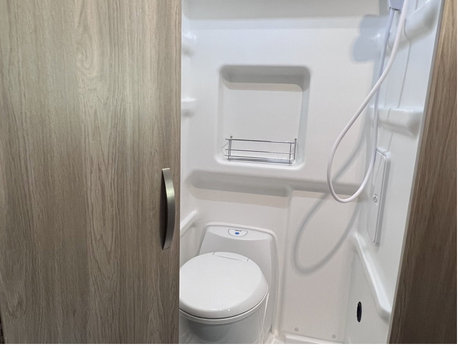 RV rental's compact wet bath: white toilet, shower head, and wood-grained cabinet. Efficient camper design.