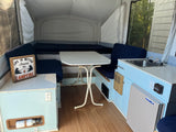 Cozy pop-up rv rental interior featuring light blue cabinets, dinette, sink, mini-fridge, and comfortable beds.