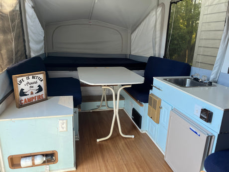 Cozy pop-up rv rental interior featuring light blue cabinets, dinette, sink, mini-fridge, and comfortable beds.