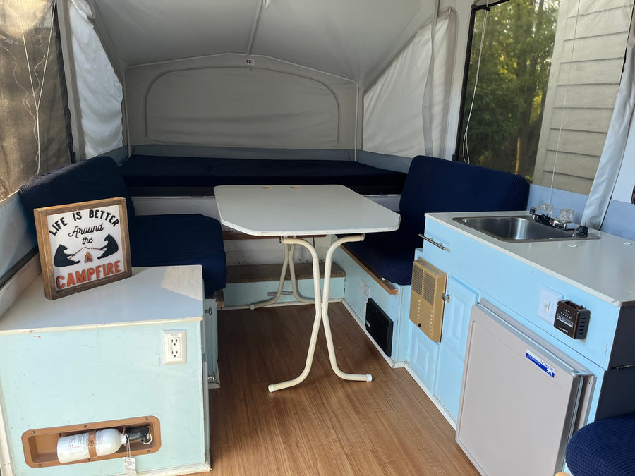 Cozy pop-up rv rental interior featuring light blue cabinets, dinette, sink, mini-fridge, and comfortable beds.
