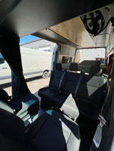 View inside a modern RV rental camper van showing three passenger seats, custom ceiling lighting, and a rear bed area.