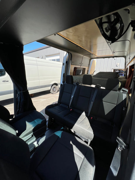 View inside a modern RV rental camper van showing three passenger seats, custom ceiling lighting, and a rear bed area.