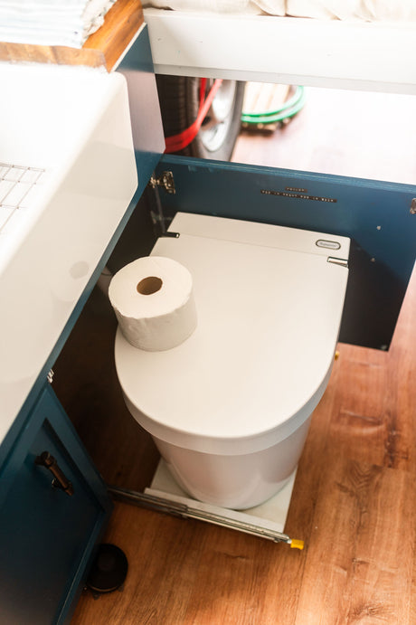 RV rental bathroom with a compact composting toilet, discreetly stored in a cabinet with usage instructions, beside a sink.