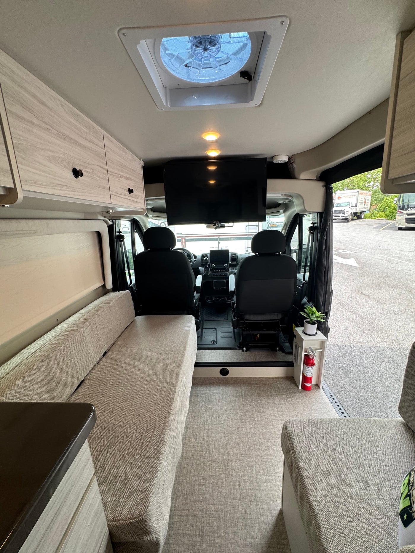 Inside a modern RV rental, showing the beige living area, cockpit, overhead TV, and ceiling fan. Ready for adventure. — photo 7
