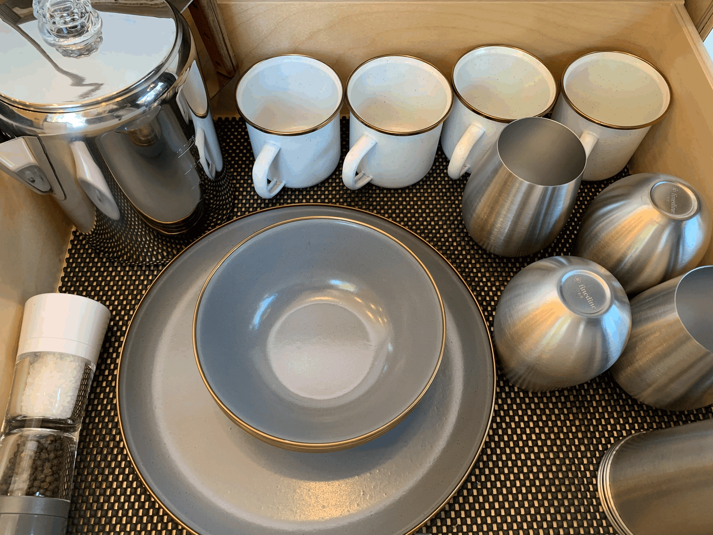 Organized kitchenware, including a percolator, mugs, plates, bowls, and salt/pepper grinders, in an RV rental.
