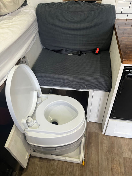 This RV rental features a hidden pull-out portable toilet, a convertible bench seat/bed, and a compact kitchen area.