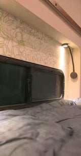 Cozy RV rental bedroom with a comfy bed, window, patterned wall, and bedside reading lamp.