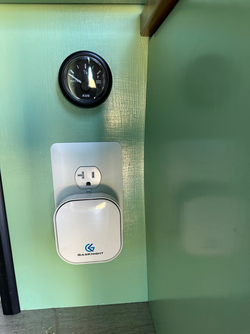 RV rental interior showing a water tank gauge, electrical outlet, and Gasknight detector on a light green wall. — photo 14