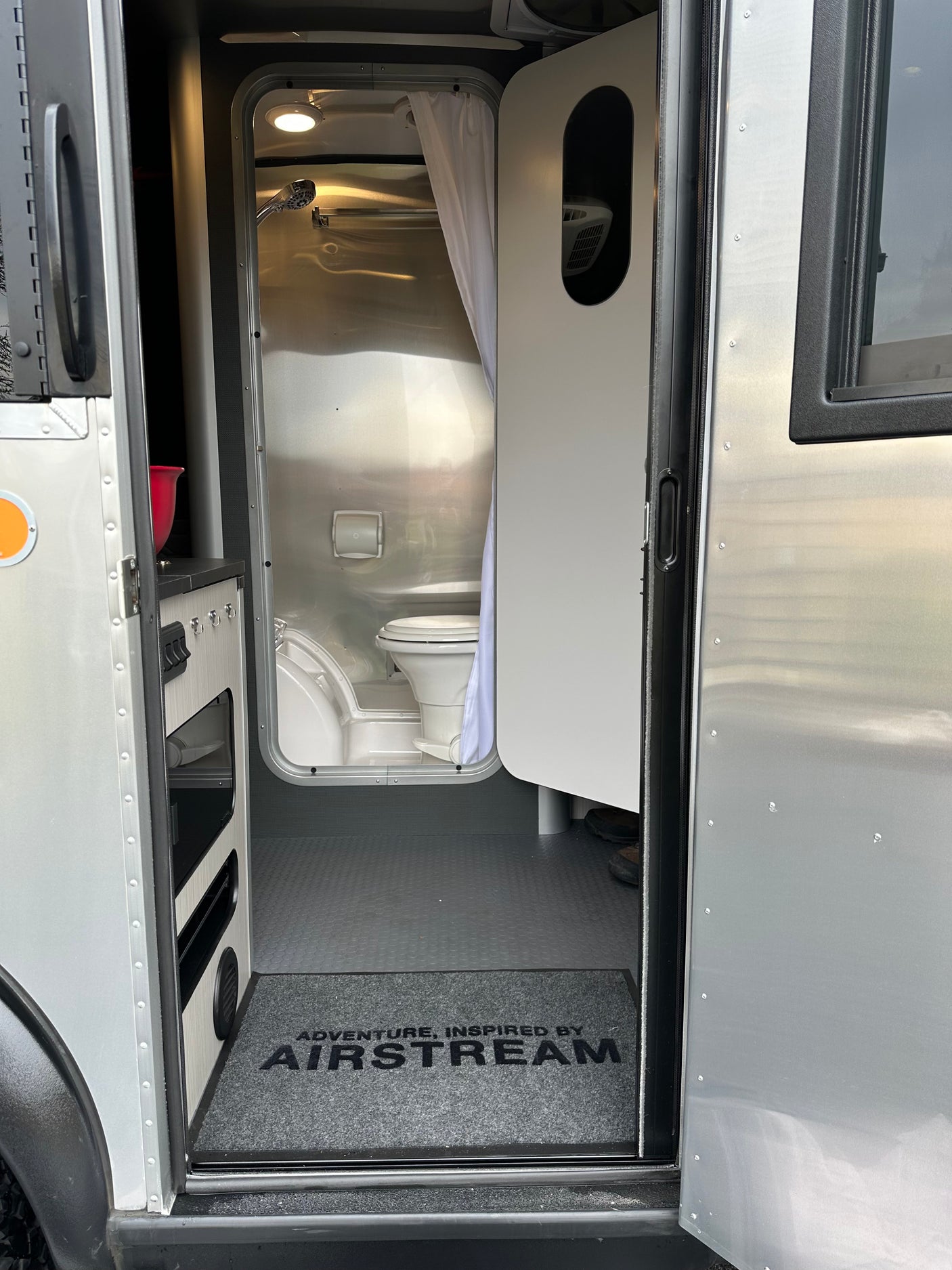 Inside an Airstream rv rental: sleek interior with compact bathroom featuring a toilet, shower, and welcome mat.