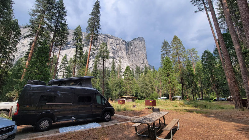 An RV rental at a Yosemite campsite, with a picnic table, surrounded by towering granite cliffs and tall pines. — photo 14
