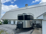 An Airstream RV rental is parked on a gravel driveway next to a barn with a metal roof under a blue sky.