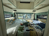Full-Size Bed with Memory Foam Topper – Sleeps two adults comfortably after a day of exploring. Bed with camping comforter, pillows, windows with curtains, and overhead storage.