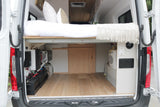 Rear view of a converted RV rental camper van, showing a raised bed over organized electrical and water systems for mobile living.
