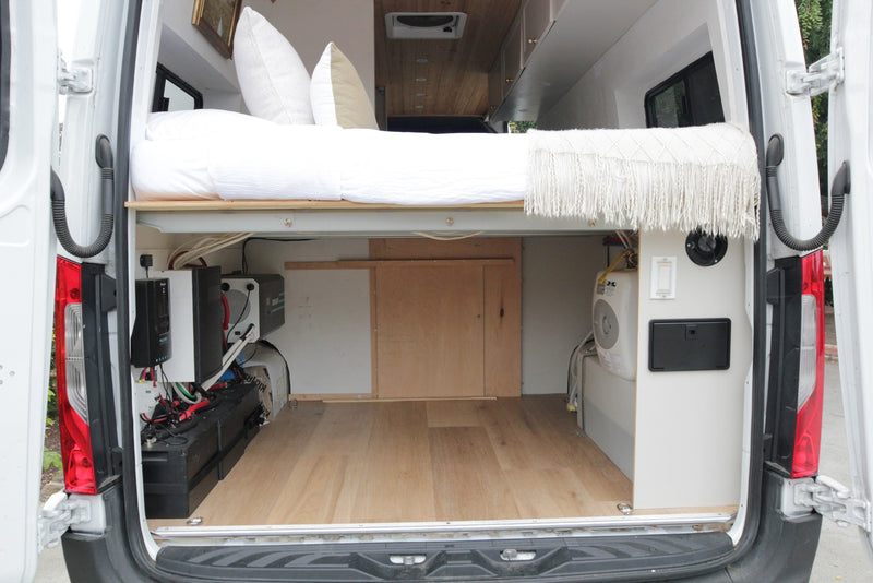 Rear view of a converted RV rental camper van, showing a raised bed over organized electrical and water systems for mobile living. — photo 8