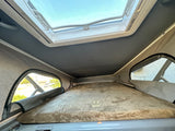 Cozy RV rental pop-top bed featuring a plush "Teddy Bear Bunk Series" mattress and a bright overhead skylight.