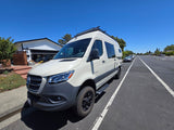 White Entegra Mercedes Sprinter RV rental parked on a sunny residential street, equipped with a roof rack.