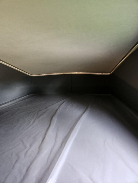 Inside an RV rental's pop-top bed: A cozy sleeping area with a light ceiling, dark sides, and a covered mattress below.