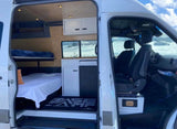 Inside this spacious RV rental camper van: multiple beds, a mini-kitchen, & driver's area. Snowy landscape visible outside.
