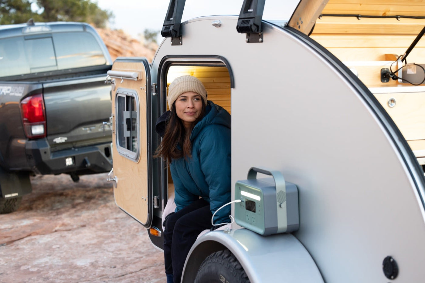  overlooking a vast desert vista at sunset. Ideal for outdoor adventures.|Stay hydrated in your RV rental! A portable Dometic faucet dispenses water into a teal cup inside a well-equipped camper.|Smiling woman relaxing in a cozy High Camp teardrop trailer. Consider this RV rental for your next camping adventure!|Cozy RV rental: woman relaxing inside a teardrop camper — photo 8