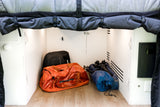 RV rental under-bed storage with an orange Patagonia duffel, black backpack, and other gear on a wood floor.