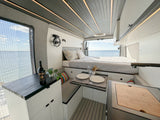 Spacious RV rental camper van interior with ocean view, comfortable bed, dining area, and kitchen setup.