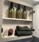 Organized RV rental bathroom cabinet: shampoo, conditioner, body wash bottles, green towels, and decorative accent.