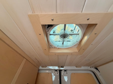 Looking up at the light wood-paneled ceiling and large, screened vent fan in this cozy RV rental interior.