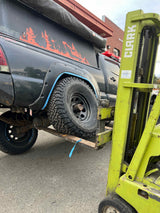 A forklift lifts an off-road truck with a camper, likely for rv rental service or maintenance. Shows BFGoodrich tires.