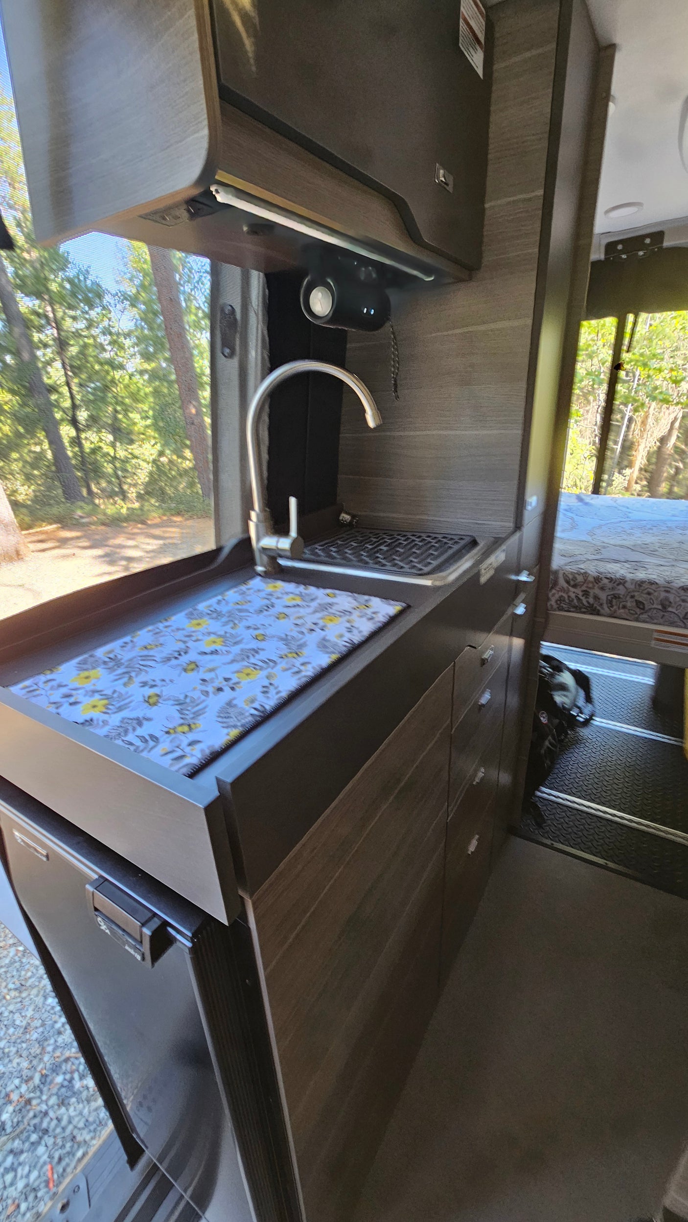 RV rental's compact kitchen: a modern sink, counter with floral mat, overhead cabinets, and under-counter refrigerator.