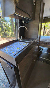 RV rental's compact kitchen: a modern sink, counter with floral mat, overhead cabinets, and under-counter refrigerator.