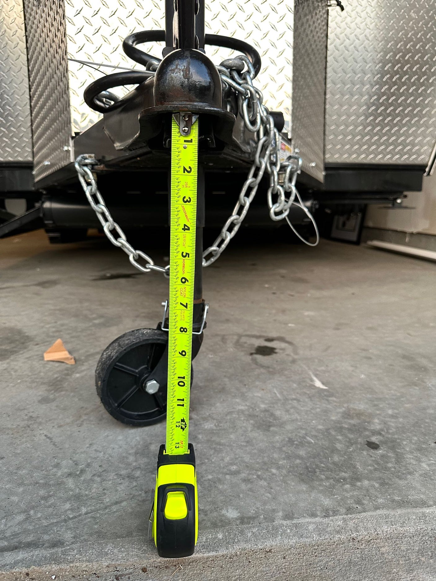 Measuring RV rental trailer tongue jack height at 12 inches (1 foot) with a tape measure, crucial for proper hitching.