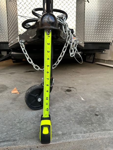 Measuring RV rental trailer tongue jack height at 12 inches (1 foot) with a tape measure, crucial for proper hitching.