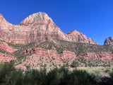 Towering red rock mountains under a clear blue sky, with sparse vegetation. Explore this majestic landscape with an RV rental.