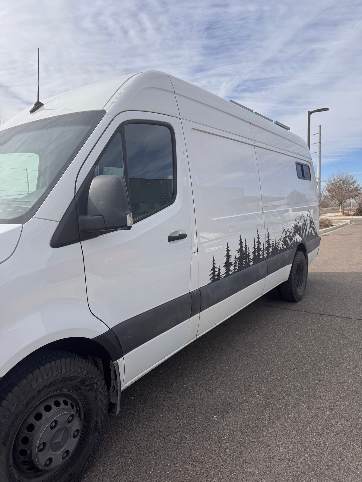 White camper van with nature (trees & mountains) decals on side, parked on asphalt. Ready for your RV rental adventure. — photo 5