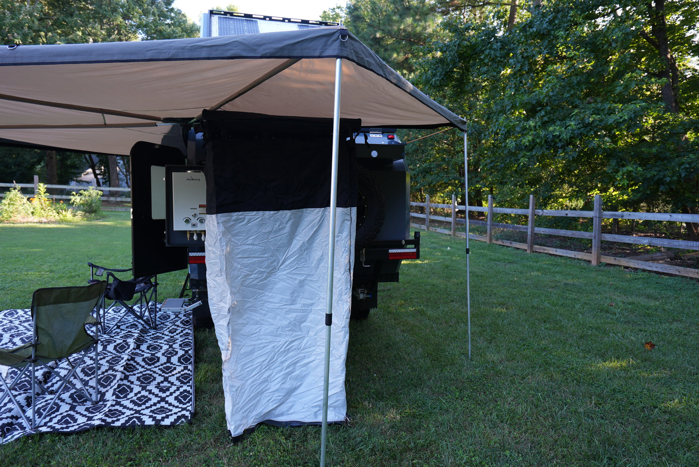 This RV rental camper trailer provides a cozy outdoor shower & awning setup with chairs and mat on the grass.