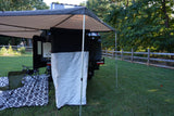 This RV rental camper trailer provides a cozy outdoor shower & awning setup with chairs and mat on the grass.
