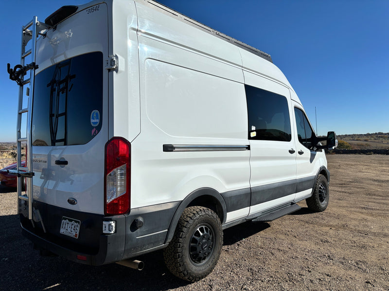 A white Ford Transit RV rental van from the rear-side view, featuring a ladder, roof rack, and rugged tires. — photo 4