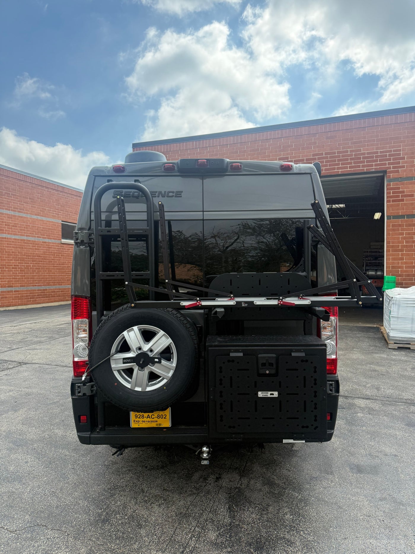 Rear of dark gray Sequence RV rental van with a ladder, spare tire, storage box, and folded bike rack. — photo 7