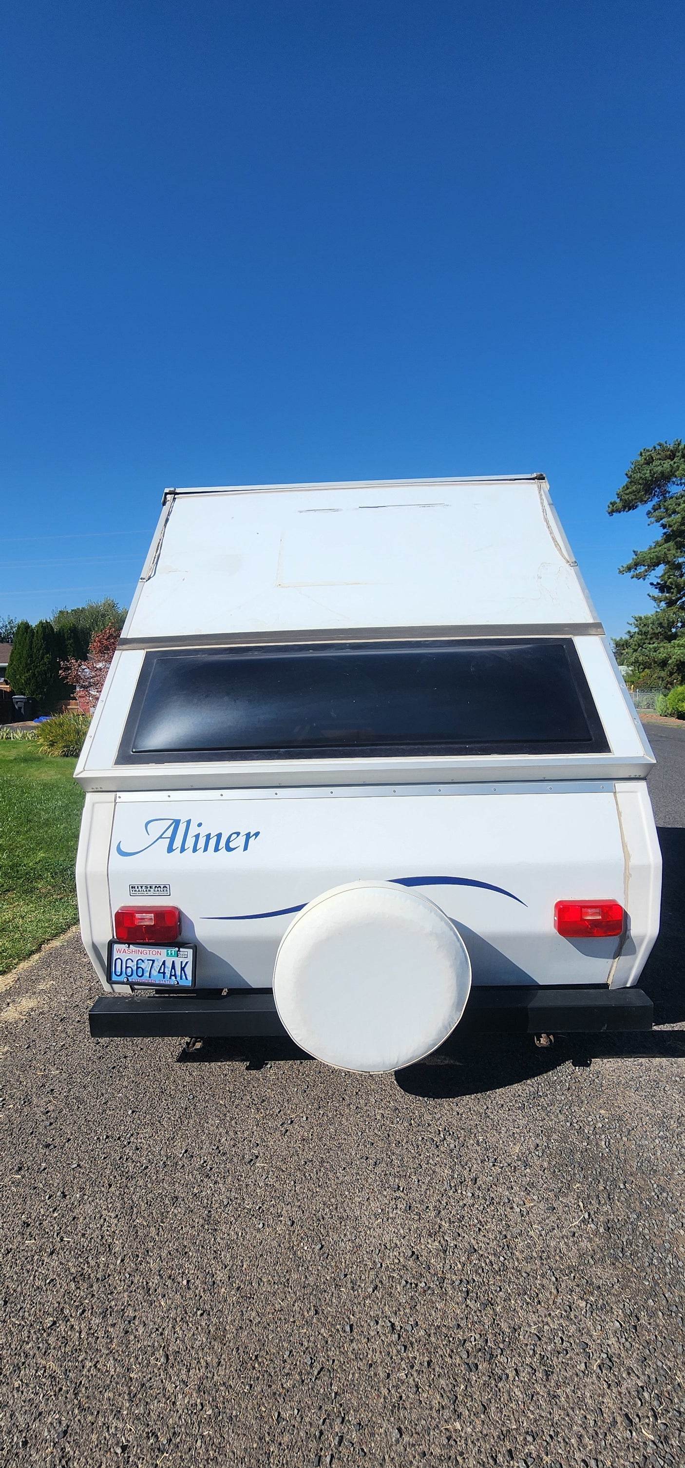 A-liner A-frame camper RV rental with WA plate 0G674AK & spare tire, parked on gravel under clear blue sky.