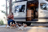 A joyful couple relaxes outside their modern RV rental van with its side door open, revealing a cozy interior.