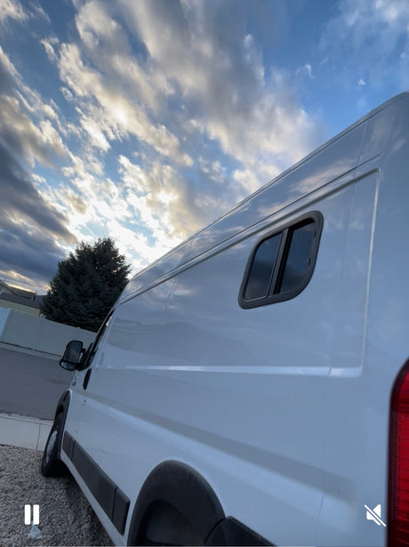Side view of a white camper van, perfect for your next RV rental adventure, shown with a custom window under a dramatic, cloudy sky.
