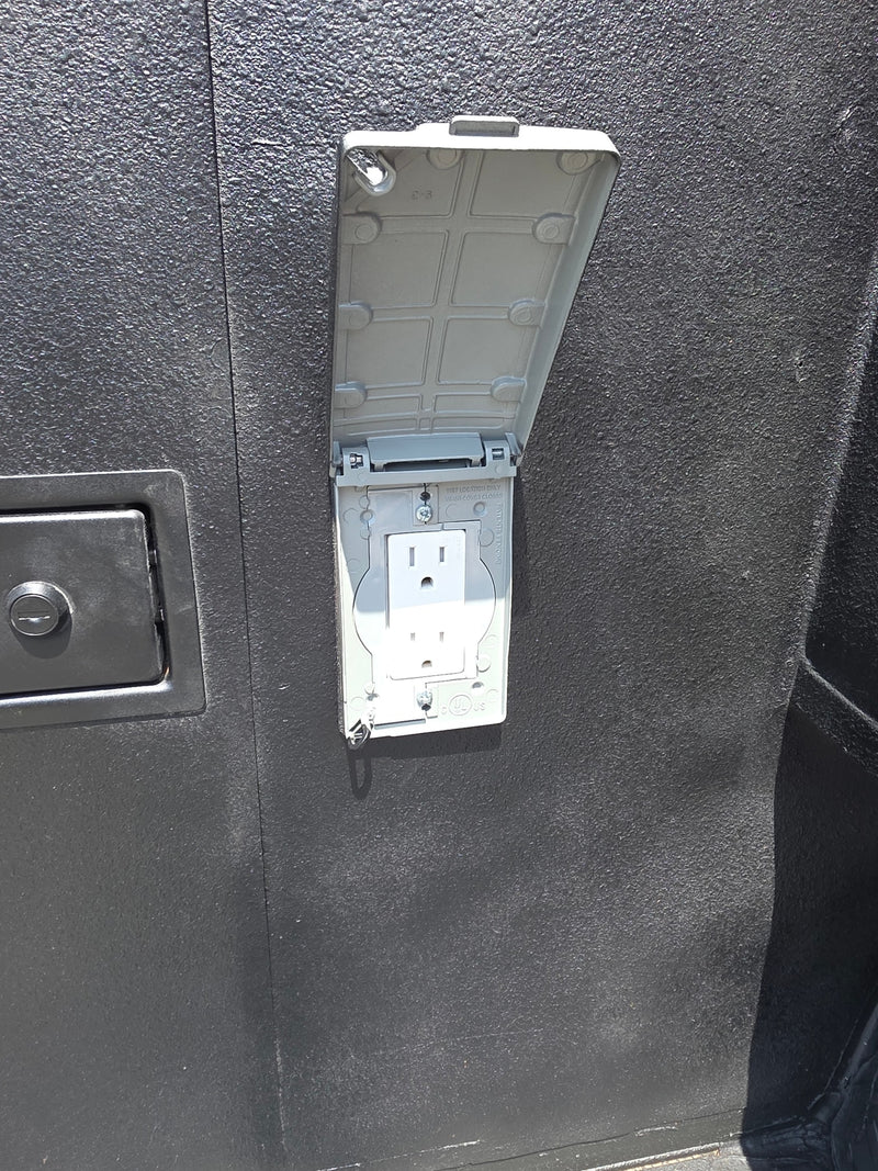 RV rental outdoor weatherproof outlet: A white 3-prong receptacle with an open gray cover on a dark, textured RV exterior. — photo 2