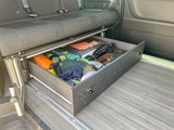 RV rental convenience: Organized pull-out storage drawer under a camper van seat, filled with camping gear.