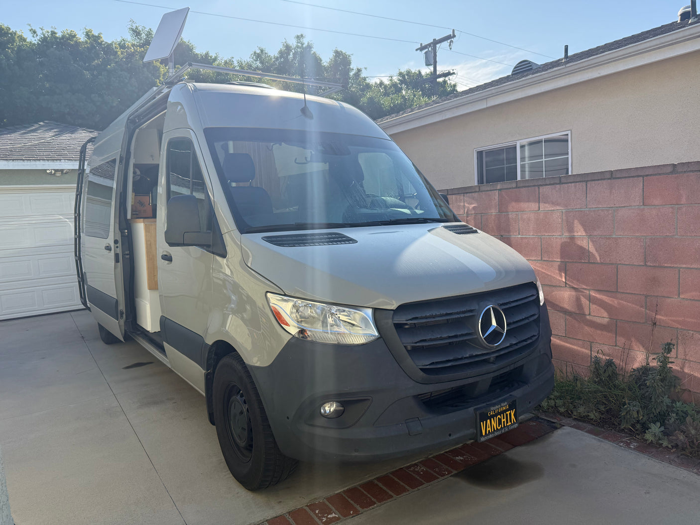 RV rental ready: Mercedes Sprinter van with Starlink antenna, door open, parked in a sunny driveway. Camper van life!