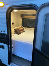 Cozy RV rental bedroom with a comfortable bed, USB charging, and an open door for fresh air. Perfect camper retreat!